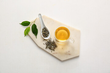 Cup of green tea and spoon with dry leaves on white background