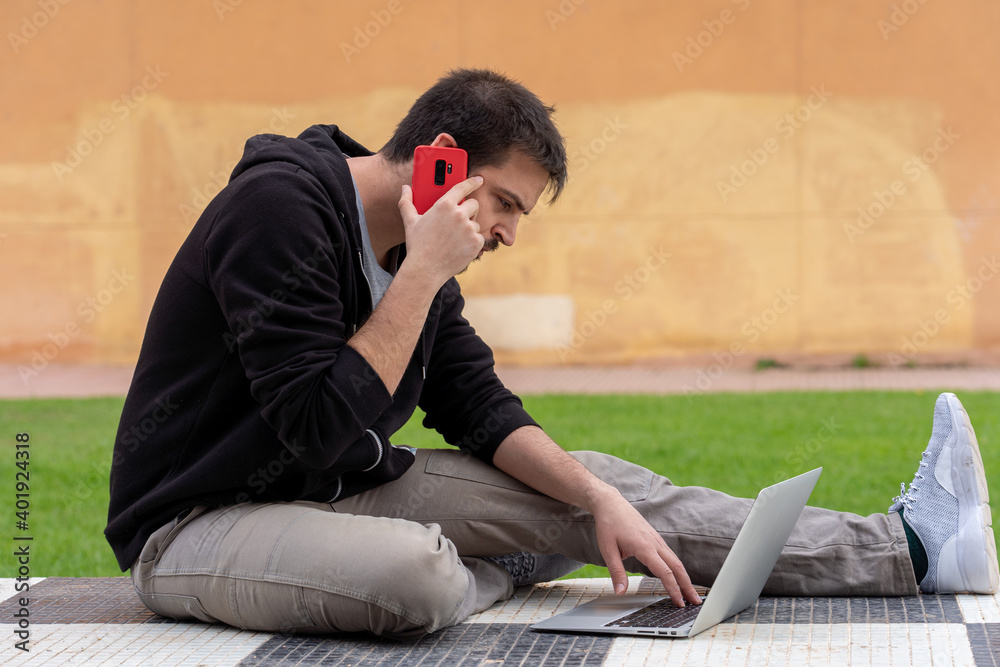 Sticker A closeup shot of a male sitting on a chess floor with a laptop and talking by telephone in hands