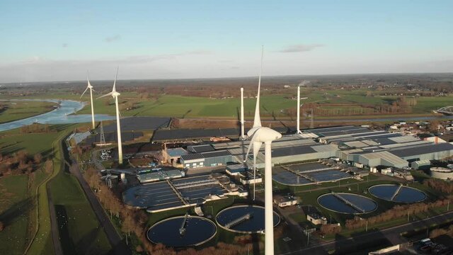 Various types of renewable sustainable energy in circular economy. Aerial with wind turbines, water purification facility, bio energy and fields of solar panels in industrial area and river landscape