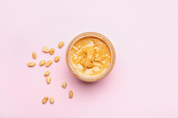 Jar with tasty peanut butter and nuts on color background