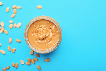 Jar with tasty peanut butter and nuts on color background