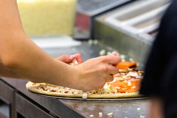 Cook in the kitchen putting the ingredients on the pizza. Production and delivery of food.