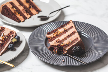 Pieces of chocolate cake with berries on gray plate, white marble background. Vegan dessert concept.