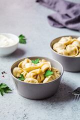 Traditional Russian meat dumplings with sour cream and parsley in gray bowls, copy space. Russian cuisine concept.