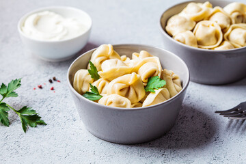 Traditional Russian meat dumplings with sour cream and parsley in gray bowls, copy space. Russian cuisine concept.