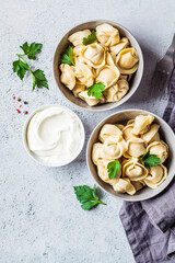 Traditional Russian meat dumplings with sour cream and parsley in gray bowls, top, view. Russian cuisine concept.