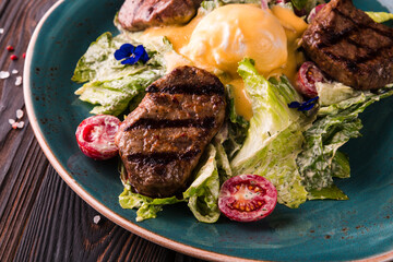 Eggs benedict with beef meat on a large white plate.. Traditional english breakfast with eggs Benedict, cherry tomato, lettuce. Benedict egg served on restaurant table background.