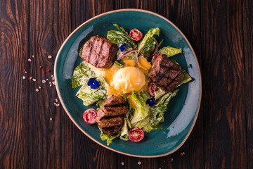 Eggs benedict with beef meat on a large white plate.. Traditional english breakfast with eggs Benedict, cherry tomato, lettuce. Benedict egg served on restaurant table background.