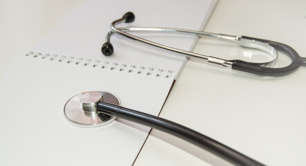 Stethoscope lies on an open empty notebook close-up at the workplace of a family doctor, a medical examination is carried out, the concept of medical care