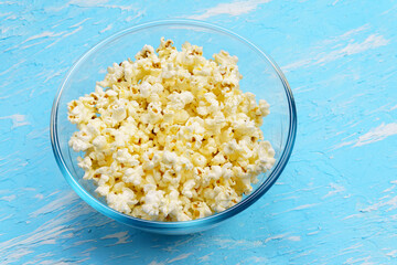 Bowl of popcorn on blue background. Leisure and entertainment concept.