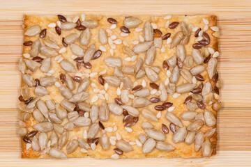 Flat flaky cookie with different seeds on a wooden surface