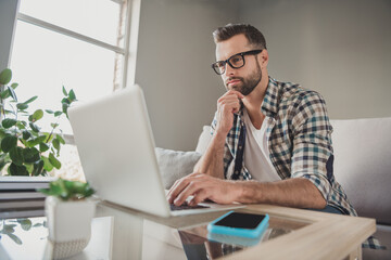 Profile side photo of young handsome man serious think look browse internet laptop sit couch home...