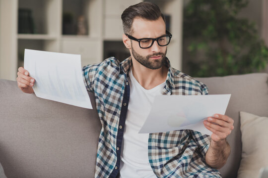 Photo Of Young Handsome Serious Concentrated Man Look Read Analyze Report Paper Documents Sit Sofa Home Remote Work