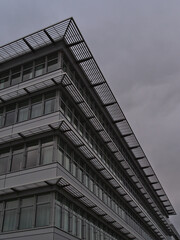 Low angle view of the facade of a modern office building with glass windows and metal elements located in a commercial park on cloudy day.