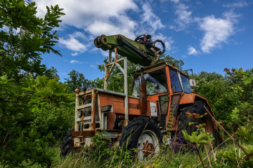 Fototapeta na wymiar old rusty tractor in the green nature with clouds on the sky