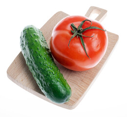 Fresh tomato and cucumber on a small wooden cutting board. Close-up image