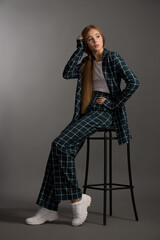 beautiful girl teenager blonde with long hair in a stylish suit in a cage posing in the studio on a gray background