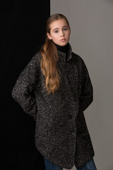 beautiful girl teenager blonde with long hair in a gray coat posing in the studio on a dark background