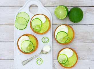 Mini lime pie topped with whipped cream and lime wedges on a light background. Top View. © Elisa