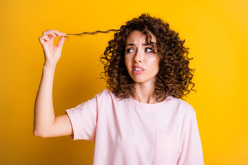 Photo portrait of unhappy girl touching curls bad hairstyle isolated on vivid yellow color...