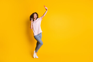 Fototapeta na wymiar Full length body size photo of female millennial taking selfie showing v-sign isolated on vivid yellow color background with copyspace