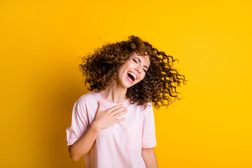 Photo portrait of woman laughing touching chest with one hand flying hair isolated on vivid yellow colored background