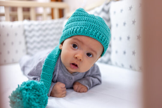A funny baby in a funny hat lies on his stomach with his head raised. Selective focus
