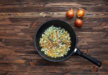 Frying pan with fried onions, three onions side by side. Brown wood background.