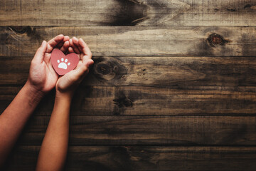 Concept of the World Day of the animal and the pets. Hands holding a heart with pet's feet. Top view with copy space.