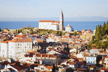 Fototapeta premium Red roofs of the historical center of old town Piran with main church against the sunset sky and Adriatic sea. Aerial view, Slovenia