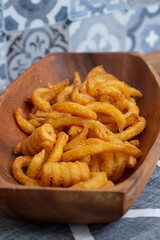Curly fries, coated in herbs and spices, in a wooden dish bowl.  Fast food concept