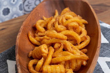 Curly fries, coated in herbs and spices, in a wooden dish bowl.  Fast food concept