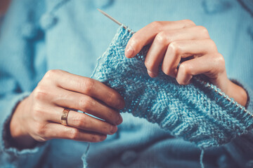close up the woman's hands knitting a blue woolen sweater