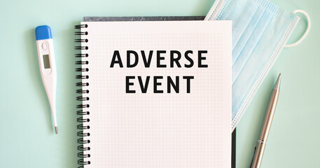 Notepad, medical mask, thermometer and pen on a blue background. ADVERSE EVENT text in a notebook.