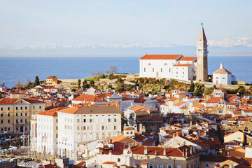 Fototapeta premium Red roofs of the historical center of old town Piran with main church against the sunset sky and Adriatic sea. Aerial view, Slovenia