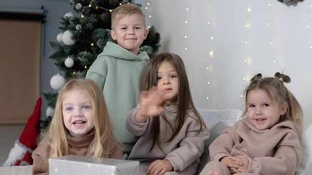 Four children showing bye-bye near Christmas tree
