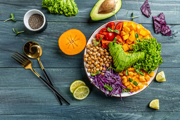 Buddha bowl vegetarian, vegan dish with avocado, tomato, red cabbage, chickpea, fresh lettuce salad, pumpkin, persimmon. Healthy balanced eating. Top view