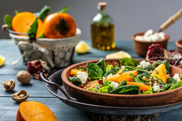 Gourmet salad with persimmon, avocado, pumpkin seeds, walnuts, pomegranate and arugula on a light background, Flat lay. Banner. Top view