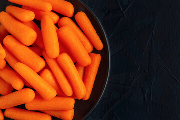 Black plate with small peeled pieces of carrot on dark textured backdrop. Top view. Space for text.