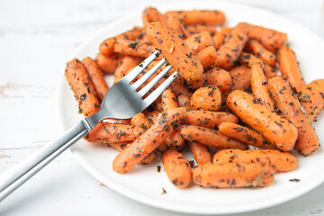 White plate with small peeled pieces of cooked baby carrot and fork on white textured wooden table