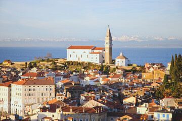 Fototapeta premium Red roofs of the historical center of old town Piran with main church against the sunset sky and Adriatic sea. Aerial view, Slovenia