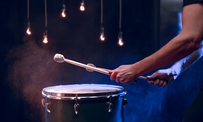 The drummer plays with mallets on floor tom in dark room.