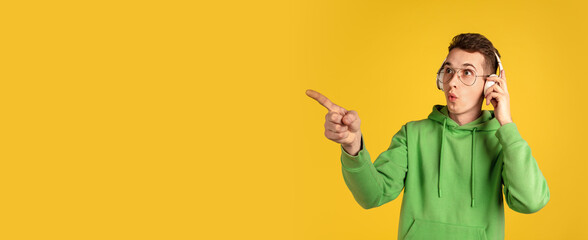 Choosing. Caucasian young man's portrait on yellow studio background. Beautiful male model in green outfit with cellphone. Concept of human emotions, facial expression, sales, ad, beauty. Flyer.