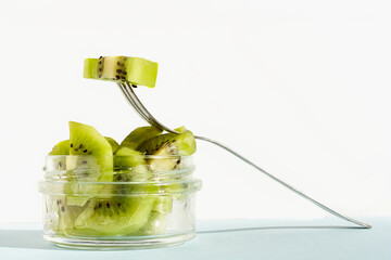 Sliced Kiwi fruits with fork in a glass bowl on turquoise pastel color background. Concept of healthy and diet food.