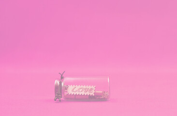 Love word inside glass bottle on pink background and copy space . Valentine's Day and Love celebration postcard concept                                