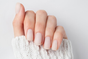 Matt nude nails close up on the light background. Winter manicure, woman hand in the warm sweater