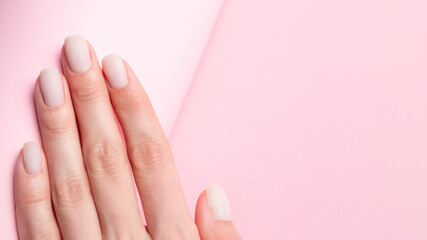 Matt nude nails close up on the trendy pink background with copy space