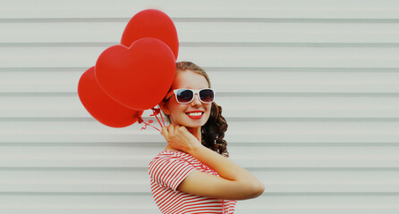 Portrait of happy smiling young woman with bunch of red heart shaped balloons on a white background