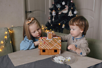 children decorate Christmas gingerbread house with paints