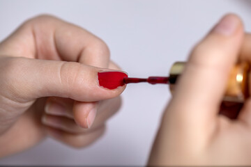 A little girl paints her nails with red varnish.